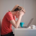 Stressed college student holding her head while studying at a laptop, illustrating AI detection anxiety