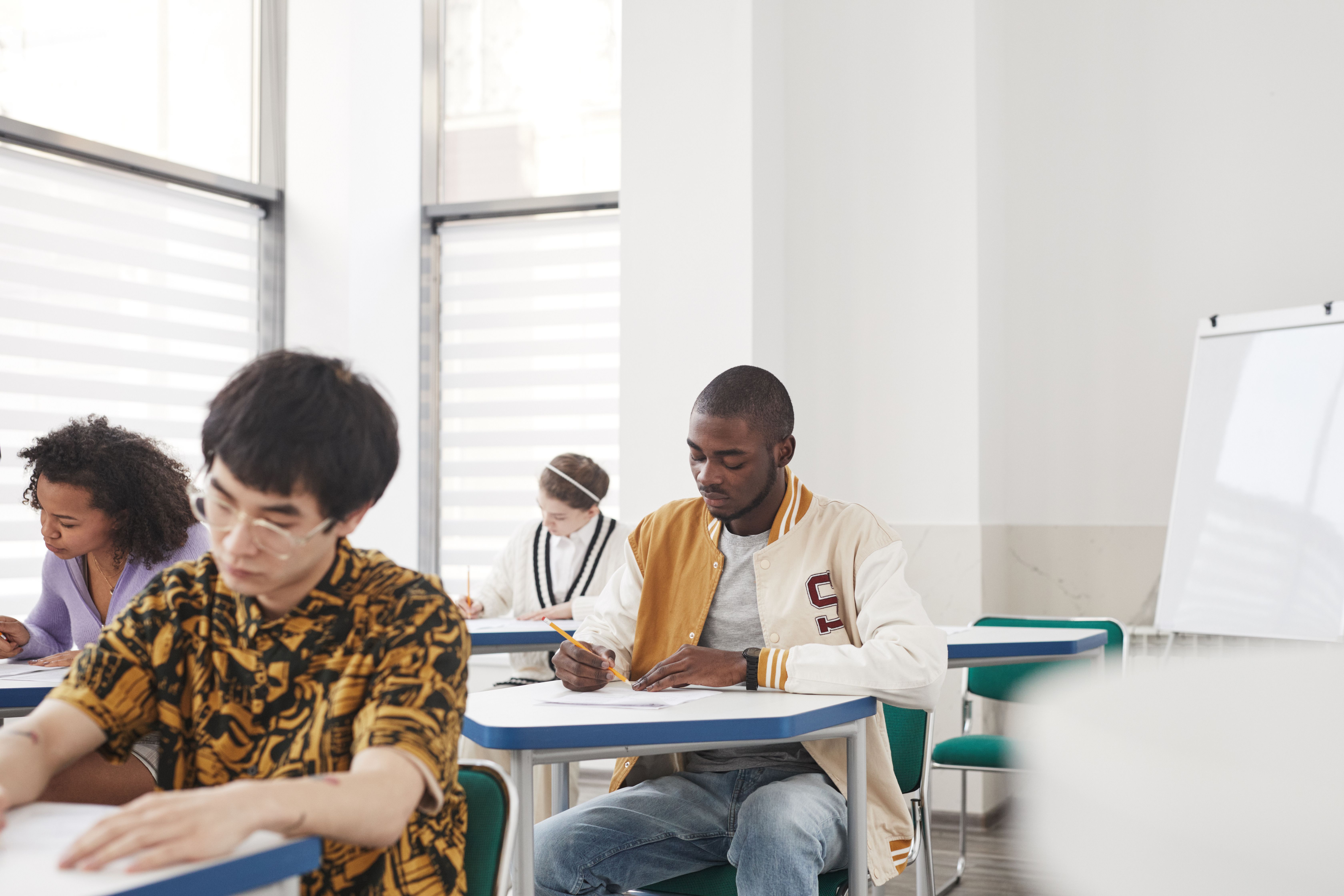 Diverse college students taking a written exam in a classroom as a way to avoid AI detection flags