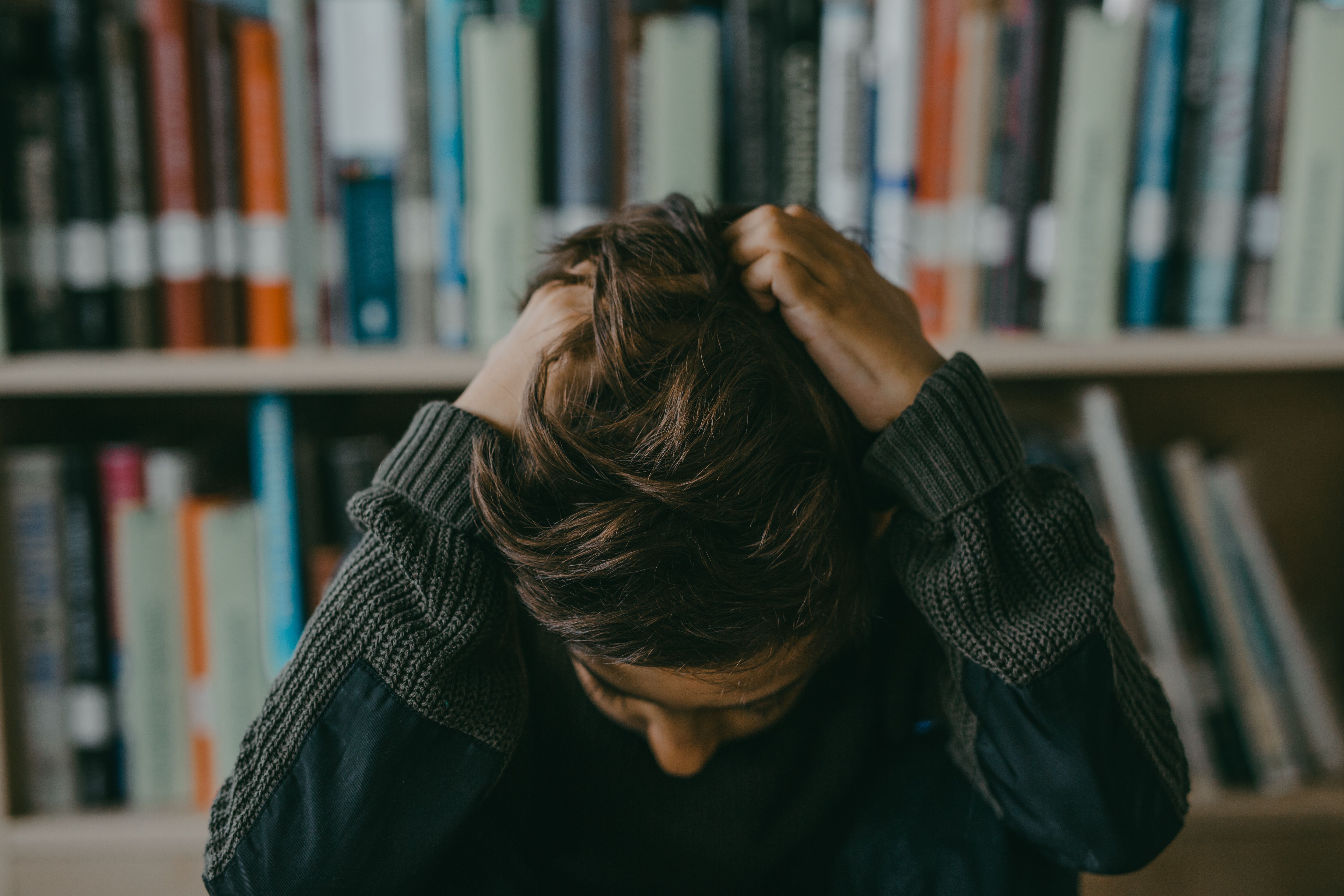 Distressed student in a library holding their head, representing academic pressure and mental health