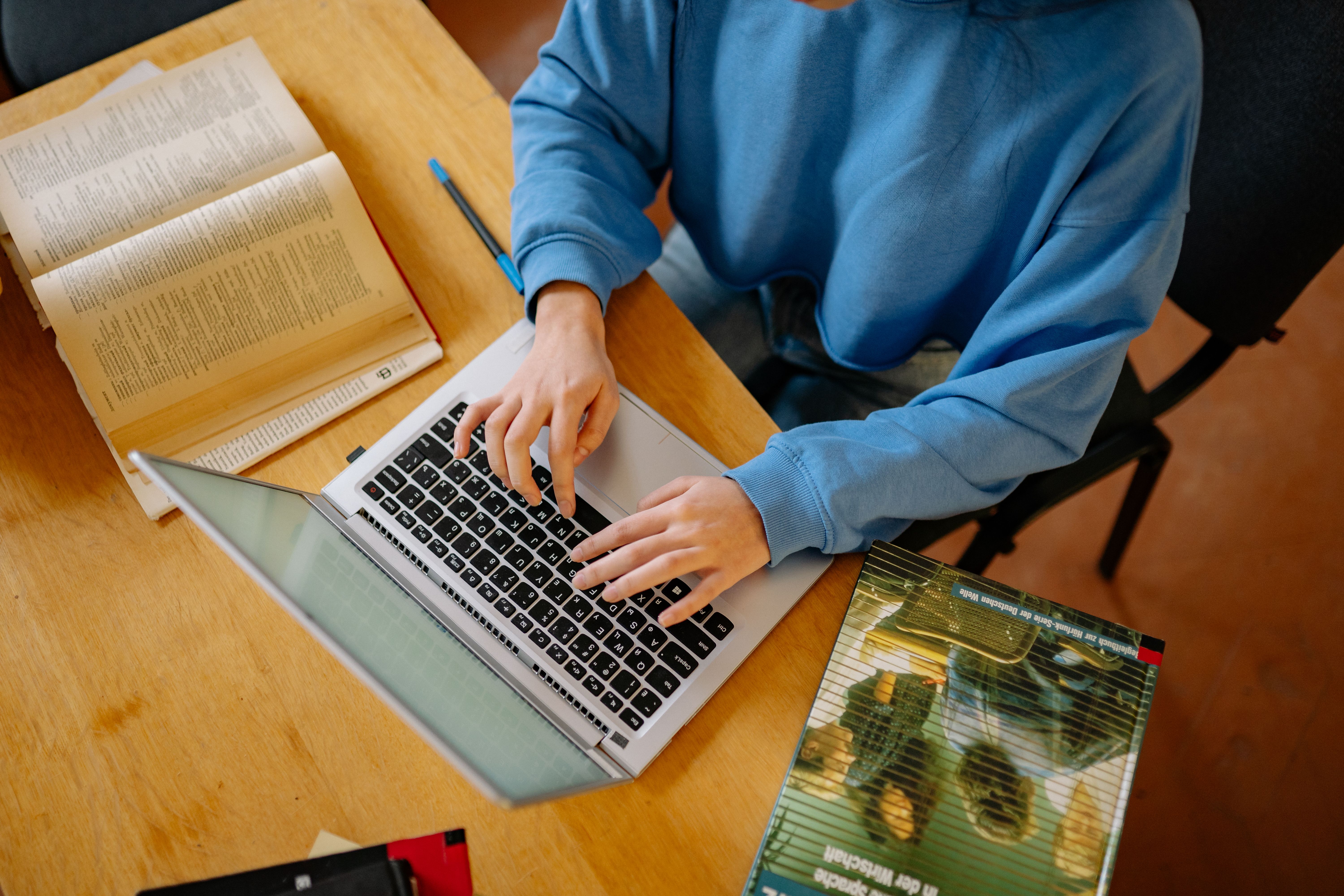Student typing on a laptop surrounded by open books while researching academic work